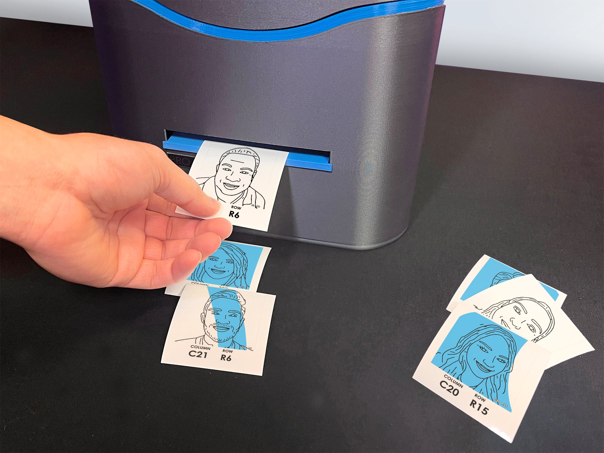 Close-up of a hand retrieving a portrait from a specialized printer, with several other portraits scattered on the table