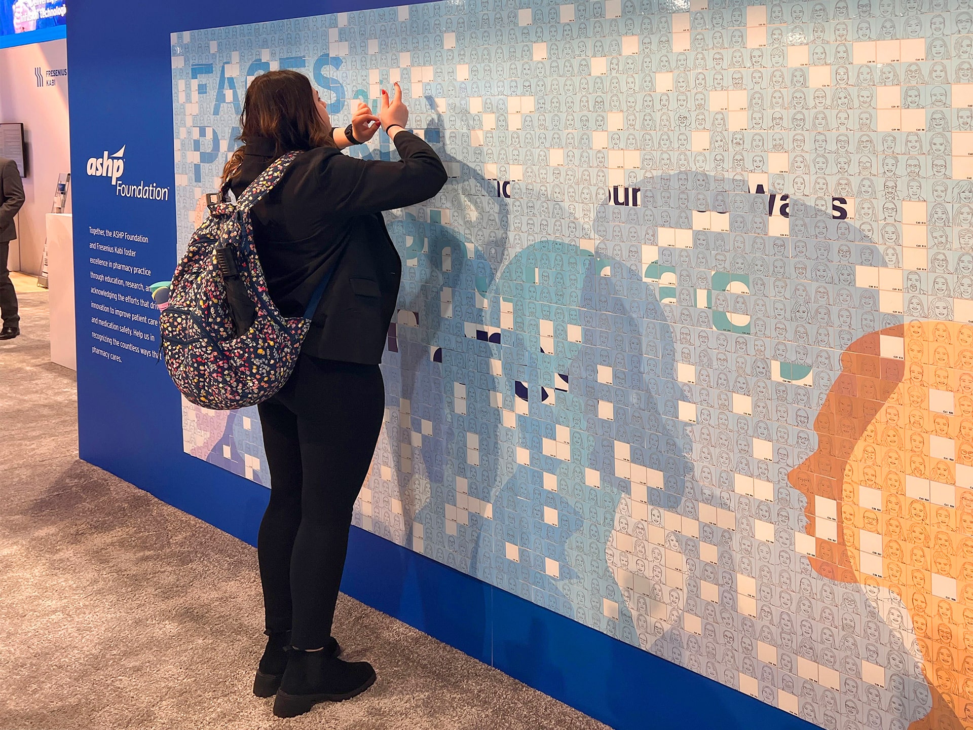 Person applying an adhesive sketch tile onto a photo mosaic wall filled with thousands of sketched portraits